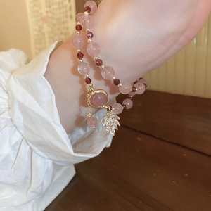 Detail of a layered pink beaded bracelet with leaf charm and natural stone pendant