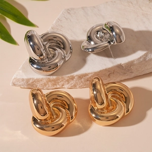 Polished gold and silver knotted metal stud earrings displayed on stone with leaf