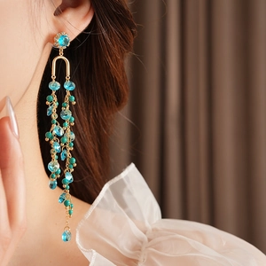 Close-up of long tassel earrings with green beads and blue stones on gold setting
