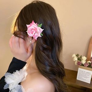 Close-up of pink gradient fabric rose flower hair clip worn on long wavy brown hair