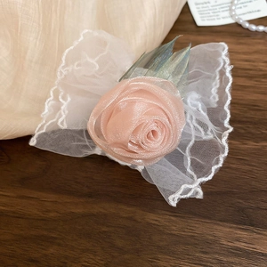 Détail d'un bracelet rose satinée avec nœud en dentelle blanche et feuilles en tulle
