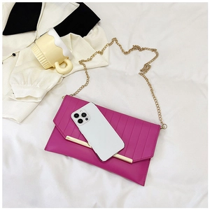 Flat lay of a fuchsia envelope clutch bag with gold trim and metal chain on white cloth