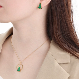 Nahaufnahme von goldenem Set aus Halskette und Ohrringen mit grünen Weihnachtsbaummotiven