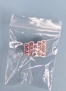 Macro detail of enamel brooch with YOU NEED TO CALM DOWN text in clear packaging