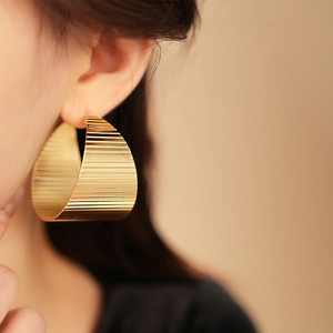 Detail view of gold metal hoop earrings with elegant textured horizontal stripes