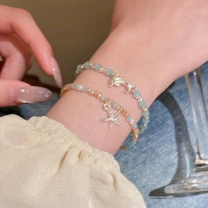 Detail von mehrlagigen Perlenarmbändern mit Delphin- und Seesternanhängern im Marinedesign