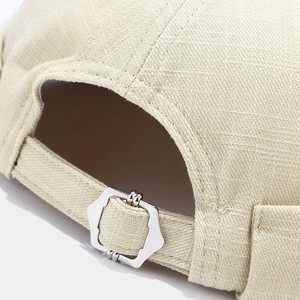 Detail of beige brimless cap featuring a metal hex buckle and textured cotton fabric