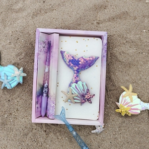 Mermaid stationery set with purple sequin notebook and pen on a sandy beach