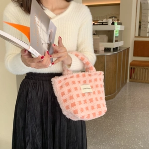 Close-up of pink and white checkered plush tote bag with brand label in a cafe setting