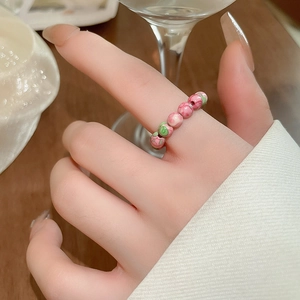 Close-up of handmade pink floral glass beaded elastic ring on finger with rustic wood background