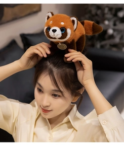 Adorable red panda plush toy with white markings and round tag held by a model
