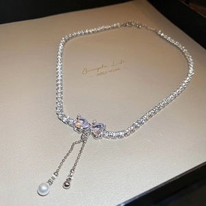 Close-up of silver bow necklace with zircon stones and elegant pearl tassel detail