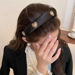 Detail of wide black satin headband featuring vintage gold heart charms on a model