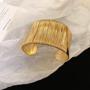 Detailed view of gold twisted wire cuff bracelet on minimalist textured backdrop