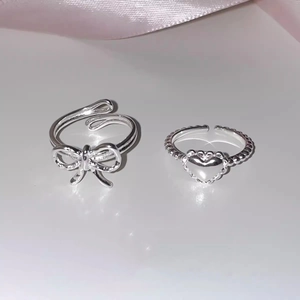 Detailed close-up of S925 sterling silver bow and heart open rings on a white surface