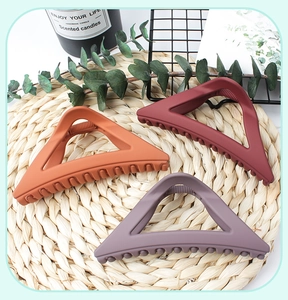 Three triangular matte hair clips in orange, dark red and purple grey on woven mat