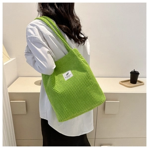 Detailed texture of green knit tote bag with white woven label on neutral background