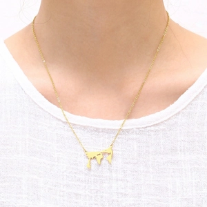 Detailed view of a gold world map pendant necklace worn on a white textured shirt