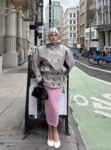 Street style view of grey double-breasted trench coat with pink polka dot skirt