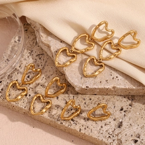Close-up of gold hollow heart earrings on textured stone and beige fabric background
