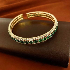 Detail of gold open bracelet featuring double rows of emerald stones and rhinestones