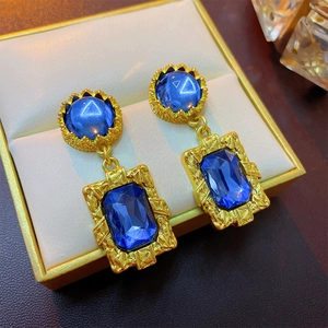 Macro view of vintage gold earrings with blue rectangular gemstones in a beige jewelry box
