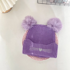 Detailed view of purple knit beanie with two faux fur pom-poms and cat heart embroidery