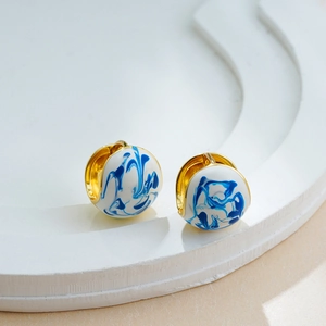 Detailed close-up of 18K gold earrings with blue and white enamel marble pattern