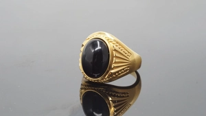 Macro view of a gold-tone signet ring featuring a large oval black gemstone with radial patterns