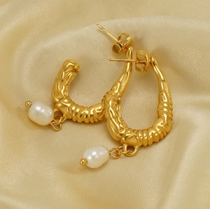 Detailed macro view of U-shaped gold textured earrings featuring elegant hanging white pearls