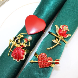 Detail of four golden metal napkin rings with red enamel hearts, roses and pearls on green napkins