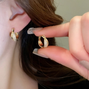Close-up of gold twisted hoop earrings with small zircon stones worn by a model