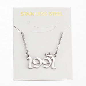 Macro detail of silver stainless steel 1991 crown pendant necklace on white card