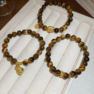 Detailed view of tiger eye stone bead bracelets with gold-tone hollow charms and pendants