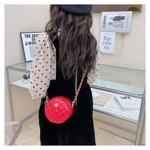 Detailed view of red quilted mini round crossbody bag with golden flower clasp worn on shoulder