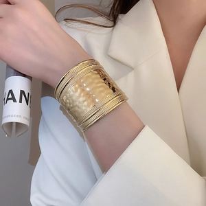 Gros plan d'un large bracelet manchette doré avec texture martelée et détails de corde