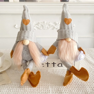 Pair of festive knitted faceless gnomes with heart patterns sitting on white props