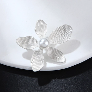 Vintage silver five-petal flower brooch with pearl center on white ceramic plate