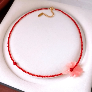 Detail of red beaded necklace with translucent pink flower pendant on white jewelry lining
