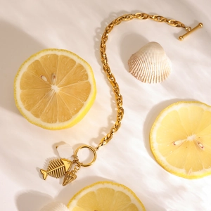 Detail of gold titanium steel bracelet with fishbone charm and OT buckle on shell background
