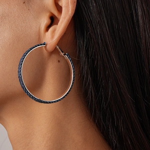 Close-up of a large blue fabric-wrapped silver hoop earring worn by a female model