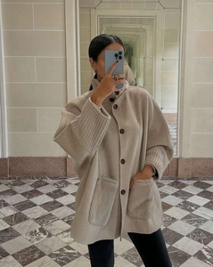 Detailed view of beige wool coat featuring plush pockets and knitted texture cuffs
