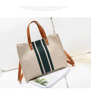 Detail of canvas tote bag with green stripe and brown leather strap on white sofa