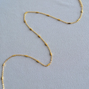 Close-up of golden necklace with rectangular metal beads on a delicate cable chain