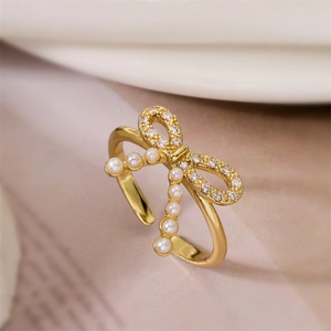 Dettaglio di un anello a fiocco dorato con strass scintillanti e delicate perle bianche