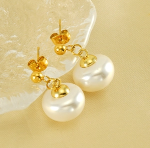 Gros plan de boucles d'oreilles perles dorées sur un plateau en verre et tissu doux