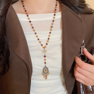 Detail of beaded long necklace with amber crystal pendant on a brown suit outfit