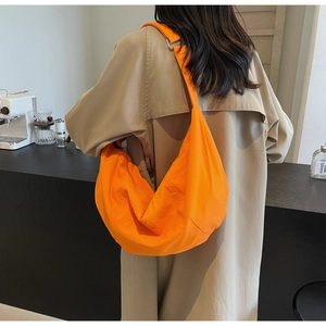 Bright orange nylon dumpling bag styled with a beige trench coat in a café setting