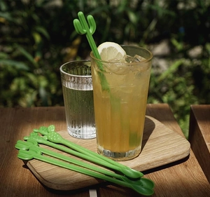 Detailed view of green cactus cocktail stirrers in a fresh lemon drink on a wooden tray