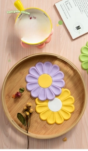 Flat lay of daisy silicone trivets in purple, yellow and green colors on a wooden tray